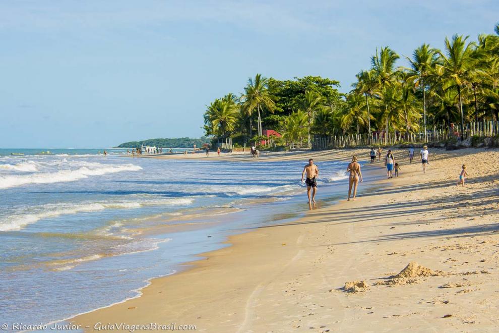 Imagem de várias pessoas camihando na beira do mar em uma tarde maravilhosa.